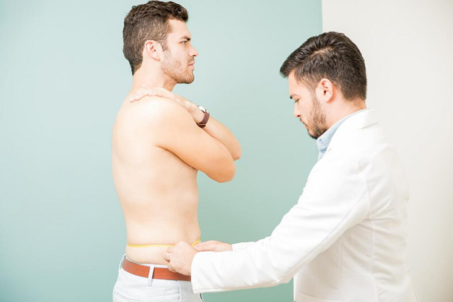 Doctor mide la cintura a un paciente.